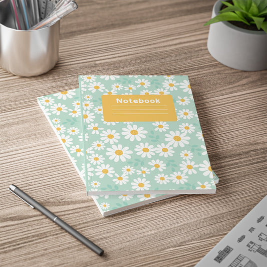 A5 floral softcover notebook with daisy print and yellow label on wooden desk with pen and plants