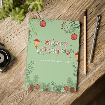 Softcover journal with Merry Christmas and Happy New Year design on green satin finish cover placed on wooden table with pencil and pen