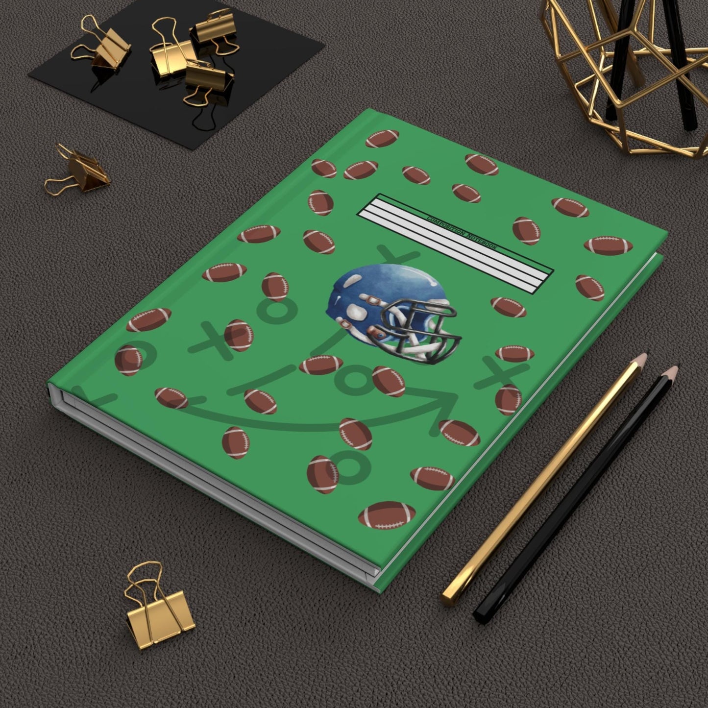 Football-themed hardcover journal with football helmet and multiple footballs design on green cover placed on table with pencils and binder clips