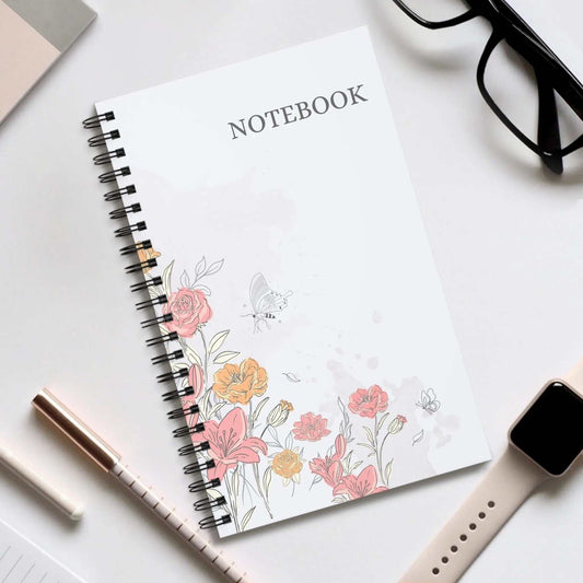 Floral spiral notebook with pink and orange flowers on white cover next to glasses, pen, and smartwatch on desk